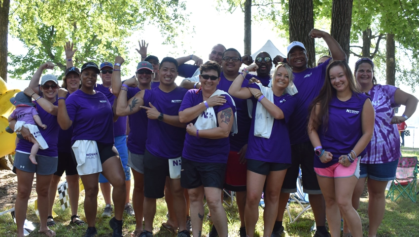 A large group of people in purple tshirts representing Novant Health, flexing their muscles for the camera.